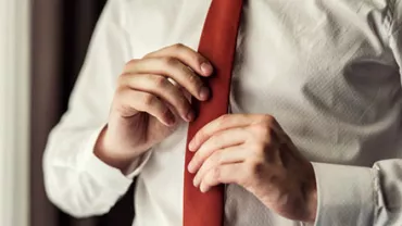 Person adjusting a red tie while wearing a white shirt.
