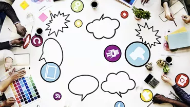 Creative team brainstorming around a table with colorful icons and sketches.