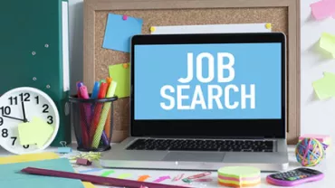 Laptop on desk with Word 'Job Search' on screen, surrounded by office supplies.