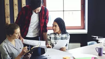 Three people discussing architectural plans at a table.