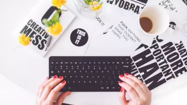 Hands typing on a keyboard with motivational posters and a coffee cup on a white table.