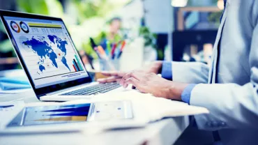 Person working on laptop with global data charts displayed on screen.