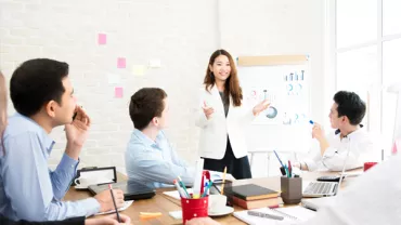 Team meeting with a woman presenting data on a flip chart.