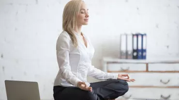 Woman meditating on desk in office attire.