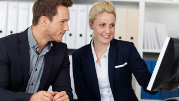 Two colleagues in suits working at a computer in an office.