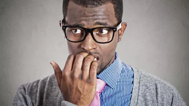 Man with glasses biting nails, looking worried.