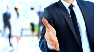 Businessman in a suit reaching out for a handshake.