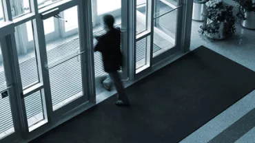 Blurred silhouette of a person exiting through glass doors.