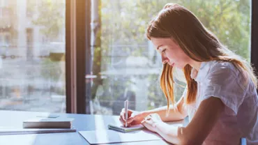 Woman writing at a sunlit desk.