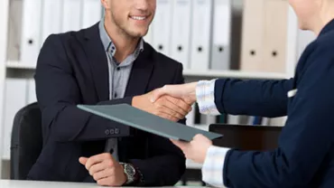 Two people shaking hands over a desk in an office.