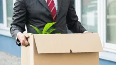 Businessman in a suit carrying a cardboard box with a plant.