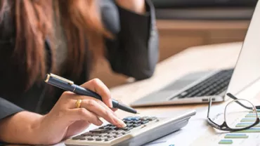 Person using a calculator at a desk with a laptop and papers.