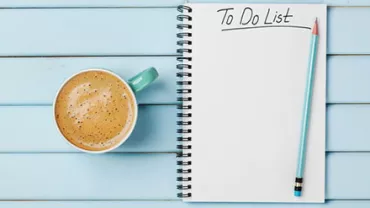 A notepad with 'To Do List' written on it, next to a cup of coffee and a pencil on a blue wooden table.
