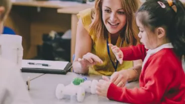 Teacher assisting a child with a toy car in a classroom setting.