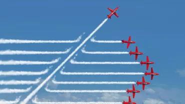 Eight red airplanes in formation, one climbing upward with smoke trails against a blue sky.
