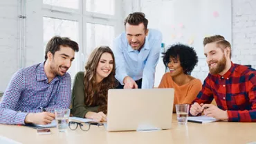 Group of coworkers smiling and collaborating around a laptop in a bright office.