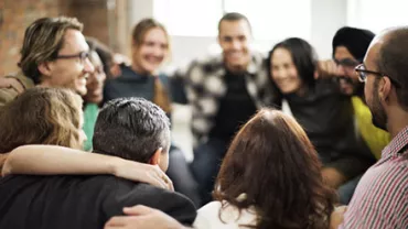 A diverse group of people sitting closely in a circle, smiling and embracing each other.