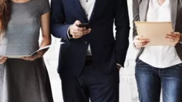 Three business professionals stand side by side holding documents and a phone.