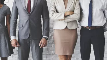 Group of professionals in business attire standing in front of a white brick wall.