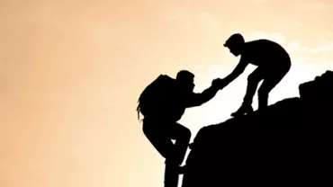 Silhouette of two climbers helping each other on a rocky cliff.