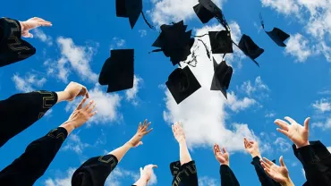 Graduates throwing caps in the air against a blue sky with clouds.