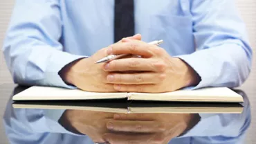 Person in a blue shirt sitting at a desk with a notebook and pen.