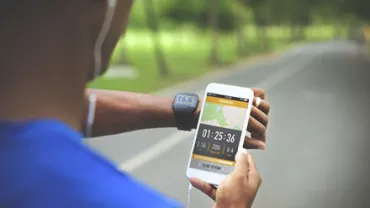 Person running with fitness tracker and smartphone, tracking activity data.