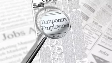 Magnifying glass over newspaper classifieds highlighting 'Temporary Employment'.