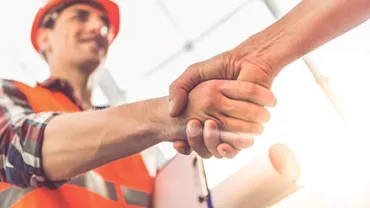 Construction worker in orange vest shaking hands with another person.