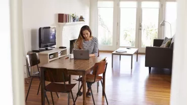 Person working on a laptop at a dining table in a cozy living room.