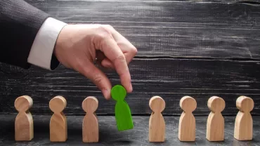 Hand selecting a green wooden figure from a row of plain wooden figures.