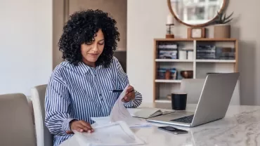 Person working at a table with documents and a laptop.