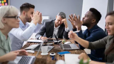 Group of people having a lively discussion in a meeting room with laptops on the table.