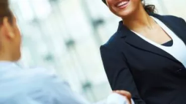 Two professionals shaking hands and smiling in a bright office setting.