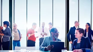 Colleagues mingling and discussing in a modern office with large windows.