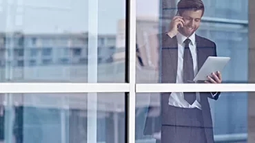 Businessman talking on phone and using a tablet by a window.