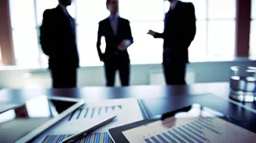 Three businesspeople discussing in an office with documents and charts on the table.