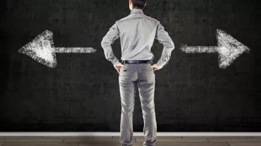 Back view of man facing two chalk-drawn arrows on a blackboard, one pointing left and the other right.