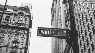 Black and white photo of Wall Street sign with tall buildings in the background.
