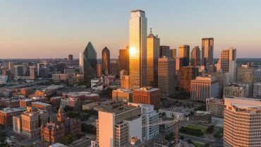 Aerial view of a city skyline at sunset, with skyscrapers reflecting golden light.