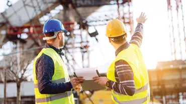 Two construction workers in safety gear discussing a building site.