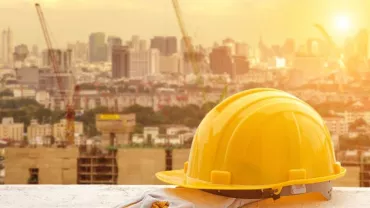 Yellow construction helmet and gloves on a ledge, city skyline in the background.