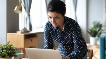 Woman in a polka dot shirt working on a laptop at a desk.