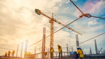 Construction workers on a building site with cranes and scaffolding under a bright sky