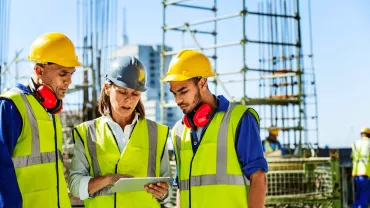 Three construction workers wearing safety gear discussing a project on site.