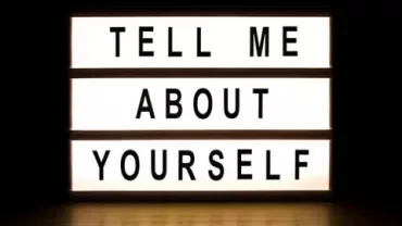 Lit sign displaying the phrase 'Tell me about yourself.'