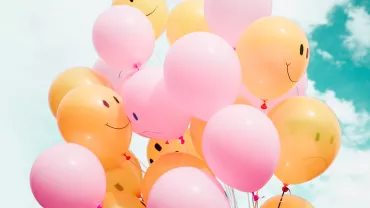 Pink and yellow balloons with smiley faces floating in the sky.