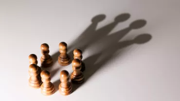 Chess pawns casting the shadow of a king.