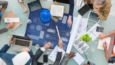 People collaborating over architectural blueprints at a table.