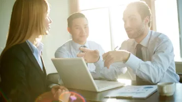 Three business professionals discussing work at a table with a laptop.